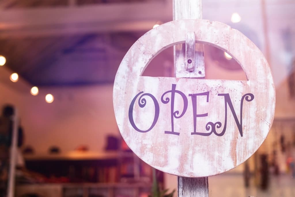 A rustic wooden 'Open' sign hanging in a small shop window